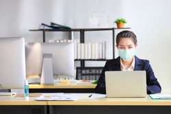 Female employee wearing medical facial mask working alone as of social distancing policy in the business office during new normal change after coronavirus or post covid-19 outbreak pandemic situation