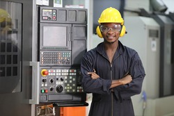 Portrait of African American mechanic engineer worker wearing safety equipment beside the automatic lathe machine in manufacturing factory