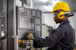 Portrait of African American mechanic engineer worker wearing safety equipment beside the automatic cnc lathe machine in manufacturing factory