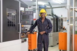 Portrait of African American mechanic engineer worker wearing safety equipment beside the automatic cnc lathe machine in the manufacturing factory