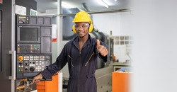 Portrait of African American mechanic engineer worker wearing safety equipment showing thumbs up beside the automatic lathe machine in manufacturing factory with copy space