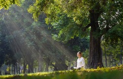 Woman relaxingly practicing meditation in the forest to attain happiness from inner peace wisdom with beam of sun light for healthy mind and soul