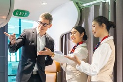 Flight attendant is welcoming and checking passenger boarding pass in business class and show him the way to his seat for airplane flight and airline transportation concept