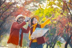 Happy Asian daughter and her senior father are walking together in public park during autumn with maple and ginkgo tree while using map for fall color travel destination and family happiness