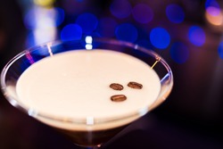 beautiful brown cocktail in martini glass with coffee and white foam closeup on a dark wooden bar counter, bokeh bright background