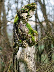 Ancient female sculpture in the forest overgrown with moss
