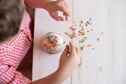 top view of Easter cake decorate children's hands with decorative dusting. Easter cake in the hands of a child on the background of a white wooden table.