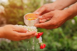 Young man's hands pour water and flowers on elder hand holding jasmine garland for Songkran festival