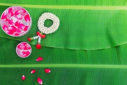 Songkran Festival background with jasmine garland Flowers in a bowl of water, perfume and limestone on a green wet banana leaf background.