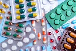 Different tablets, pills in foil blister packs, medications drugs on blue background