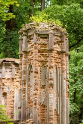 Elements of ruins of mighty castle in the forest, green trees all around. Demolished building of the past, remains of brick edifice, vertical photo.