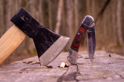 Hatchet or ax and folding pocket knife stuck upright in a tree stump outdoors in a garden or woodland conceptual of an outdoor lifestyle or camping