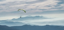 A paraglider soars in the sky over the foggy Carpathian valley. Paragliding. Concepts: adventure, determination, extreme sports. Alpine ski resort. Rest in Ukraine, Carpathian.