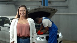 Mechanic repairs a car, woman smiles at the camera 