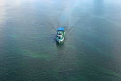 A fishing boat sails along a calm river or sea. Top view.
