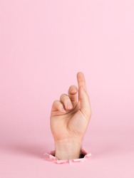 Male hand sticks out of a hole in paper, on a pink background. Indicates sign, copy space.
