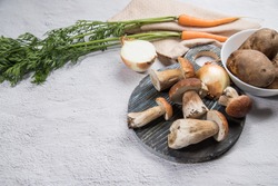 Various ingredients for cooking forest porcini mushrooms are laid out on a light background-mushrooms, carrots, potatoes, onions, with a round cutting Board. Horizontal . Place for copy space