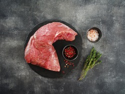 Raw beef tri-tip steak for BBQ on wooden board with salt, garlic and pepper, top view