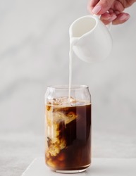 Iced coffee in a tall glass with cream poured over. Cold black coffee with ice cubes in a high glass pour cream.