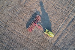 Aerial view of a tractor with a trailed cultivator processing arable land before sowing grain crops.