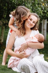 portrait of loving mother and two adorable kids. little girl and newborn baby girl with mom outdoors on summer day. Happy family spent time together in the park