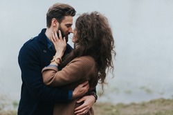 Happy lovers near the lake. Young couple is hugging on autumn day outdoors. A bearded man and curly woman in love. Valentine's Day. Concept of love and family