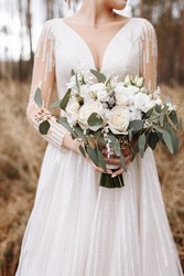 wedding accessories. bride is holding a Lush wedding bouquet of white roses and greenery outdoors on wedding day. woman in a long white dress . High quality photo.