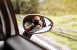 man takes photo in mirror in car. A man is taking photo someone or something from an open car window. Reflection in the side mirror of the car.