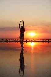 silhouette of a young slim woman in a swimsuit who dancing at sunset on the sea. summer holiday.