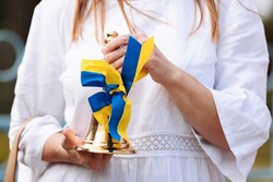 cropped photo of female hands holding school bell with a blue yellow bow - a symbol of the beginning of the school year or graduation in Ukraine. Concept of education. Back to school