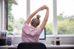 Rear View Of Woman Working From Home On Computer  In Home Office Stretching At Desk