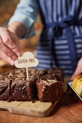 Sales Assistant In Bakery Putting Gluten Free Label Into Freshly Baked Chocolate Brownies