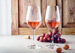 Two glasses of rose wine and a bunch of grapes on a light wooden background.
