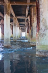 underside of pier with old rusty concrete pillars with ocean water and sand