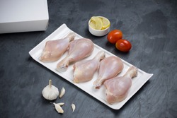 Raw chicken drum sticks arranged on white table ware with small tomato,garlic and lemon slices with delivery box on stone textured or graphite colour background