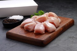 Raw chicken tender fry cut without skin arranged on wooden board and garnished with coriander leaves,salt and black pepper with delivery box on stone textured or graphite colour background