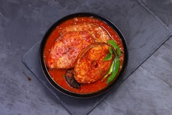 Seer Fish curry, traditional Indian fish curry ,kerala special ,arranged in a black bowl garnished with curry leaves and fresh green chilli on a grey textured background,isolated top view.