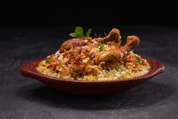 Chicken dhum biriyani using jeera rice and spices arranged in  earthen ware with raitha and lemon pickle  on grey background.
