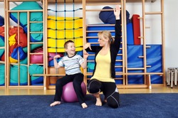 Woman as a therapist at physiotherapy with medicine ball with child in gym