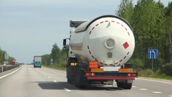 Semi truck with propane tank moving on asphalt road on a summer day - ADR dangerous cargo, side rear view