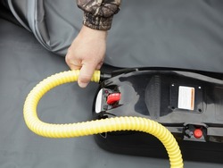 A man hands connects the hose to automatic electric air pump for pumps up in inflatable boat closeup