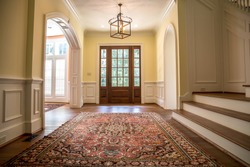 Grand and elegant yellow entrance to a home with stairs. Oriental rug a wood and glass window door.