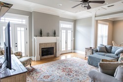 a bright and airy neutral beige gray living room den in a new construction house with a white and tiled fireplace as the main focal point as well as a decorative rug and lots of natural window light.