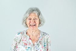 Elderly woman in her 80's with Gray hair isolated on a white backdrop smiling and laughing and happy.
