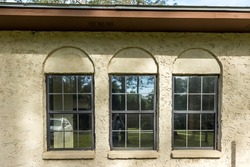 The side view of a brown ranch style spanish style villa stucco cinder block home with architectural arches and black aluminium original windows.