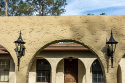 The top front view of a brown ranch style spanish style villa stucco cinder block home with architectural arches and black aluminium original windows.
