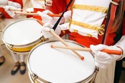 Young girls drummers hands in red uniforms and white skirt with white gloves drumming on drums at marching band
