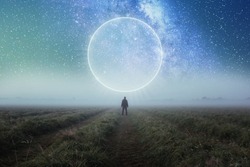 A science fiction concept. A man standing in a field looking out across space with a glowing portal in the night sky