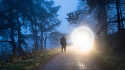 A man looking at a mysterious glowing portal  on a forest road on a foggy winter evening.