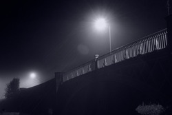 Looking up at the railings on a bridge. Illuminated by street lights. On a atmospheric foggy night.